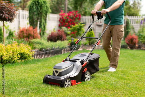 Close-up of man with lawn mower cutting green grass in modern garden on his backyard. New modern lawn mowing machine