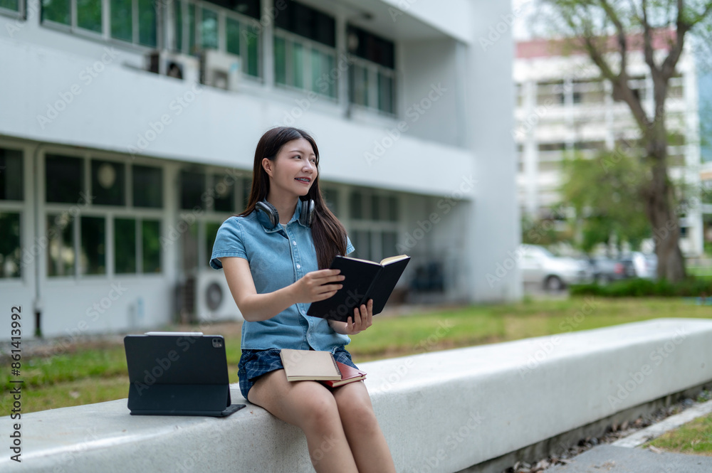 Fototapeta premium A woman is sitting on a bench with a laptop and a book