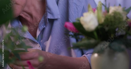 Female florist's hands remove extra petals from bud of flower. Close-up of basket full of spring pink flowers. Vertical video format