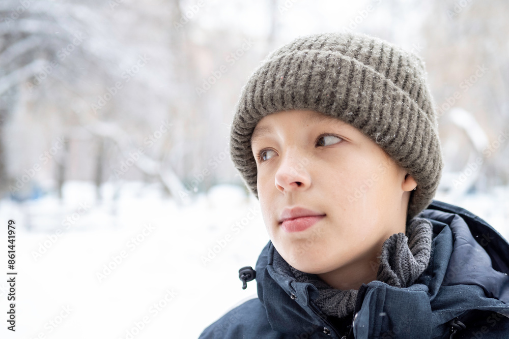 Young Caucasian boy wearing a knitted hat and winter jacket looking to the side outdoors in a snowy landscape Young Caucasian boy wearing a knitted hat and winter jacket looking to the side outdoors in a snowy landscape