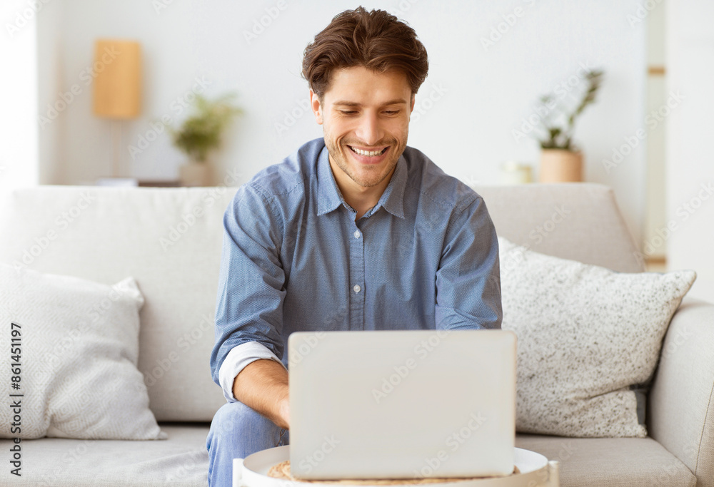 A man sits on a couch and smiles while using a laptop. A man sits on a couch and smiles while using a laptop.