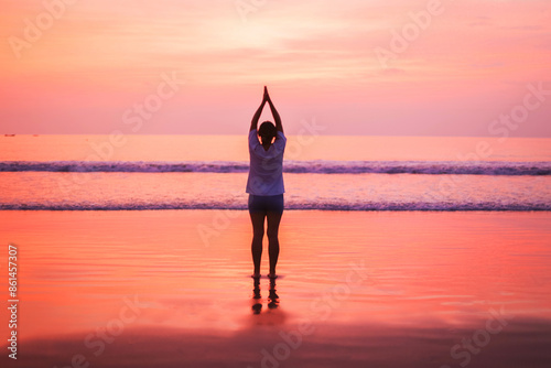 A young woman meditates against the background of a bright red sunset. Creative concept of yoga classes on the beach near the ocean