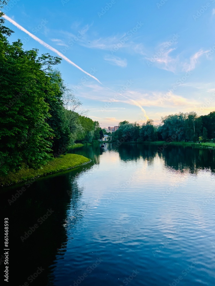 Sky and trees reflection on the calm surface of the lake, summer lake in the park, green trees, blue sky with tender clouds Sky and trees reflection on the calm surface of the lake, summer lake in the park, green trees, blue sky with tender clouds