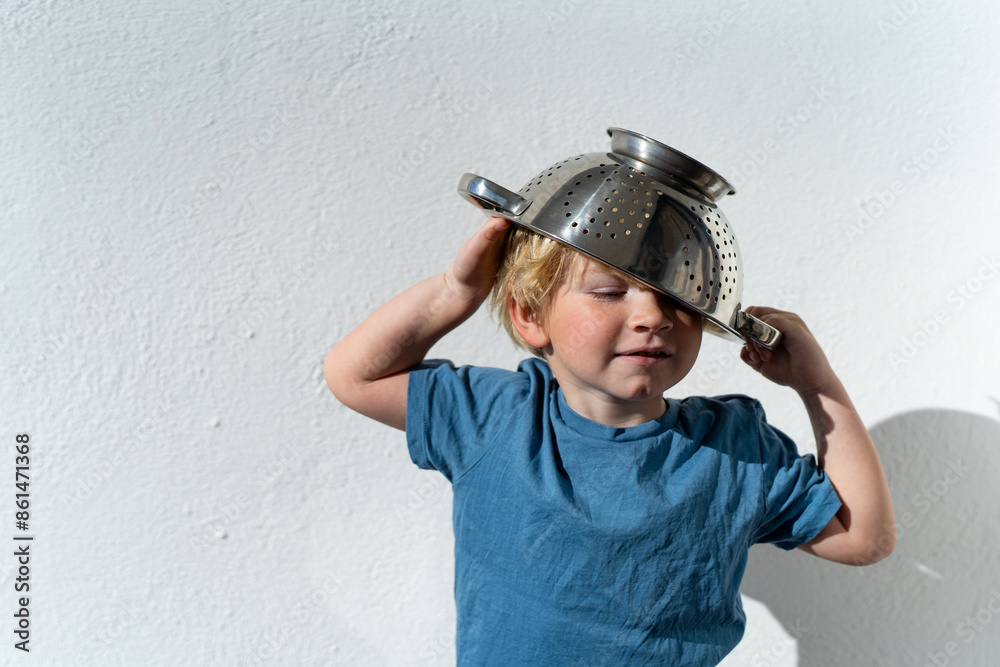 Little boy putting colander on his head . cheerful blond boy with a sieve on his head. positive kid Little boy putting colander on his head . cheerful blond boy with a sieve on his head. positive kid