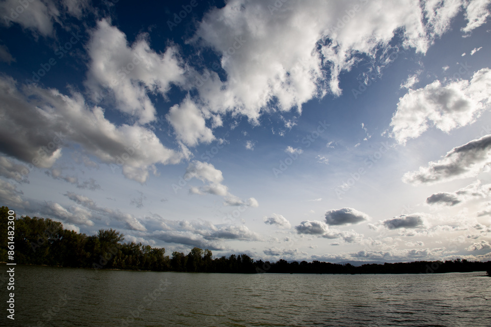 River with autumn foliage and cloud-filled sky, showcasing serene landscape and seasonal natural beauty River with autumn foliage and cloud-filled sky, showcasing serene landscape and seasonal natural beauty