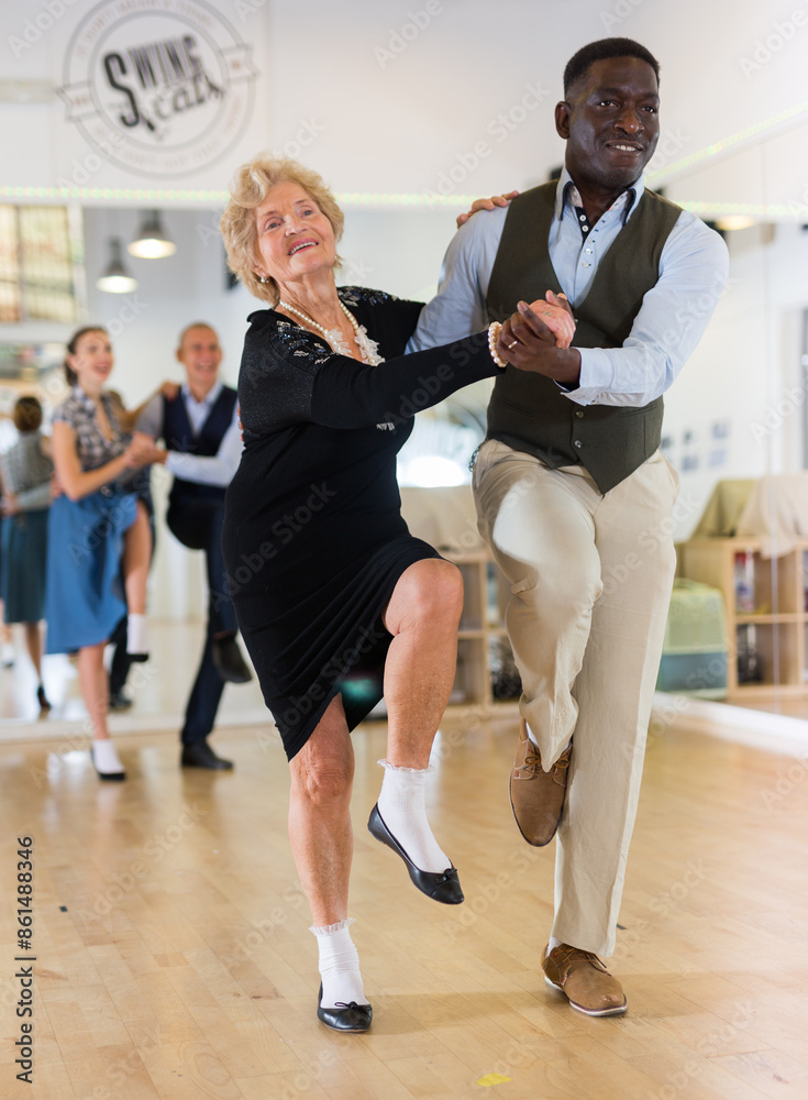 Man and elderly woman performing jazz dance in dancing room