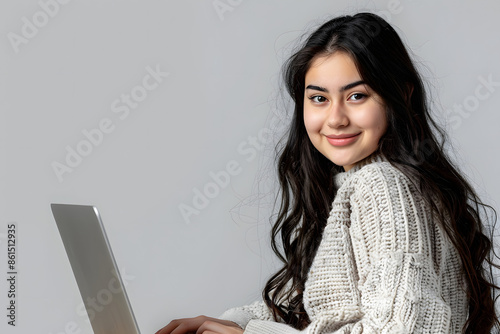 A young woman working on a laptop against a solid grey background 