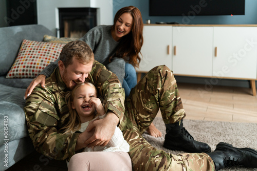 Overjoyed soldier tickling small daughter while sitting at home at the floor
