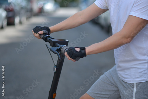 A man with an electric scooter. Close up photo of hands in sport gloves on the steering wheel. The concept of ecology and healthy lifestyle in the city