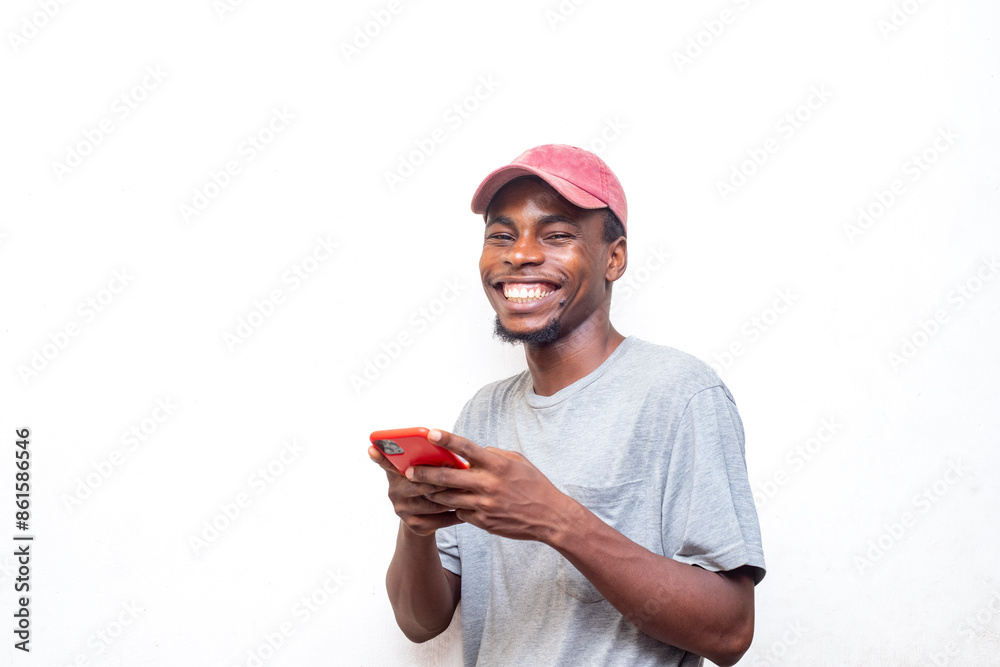 Smiling young man in casual attire and cap using a smartphone against a white background. Concept of joy, technology, and communication. Smiling young man in casual attire and cap using a smartphone against a white background. Concept of joy, technology, and communication.