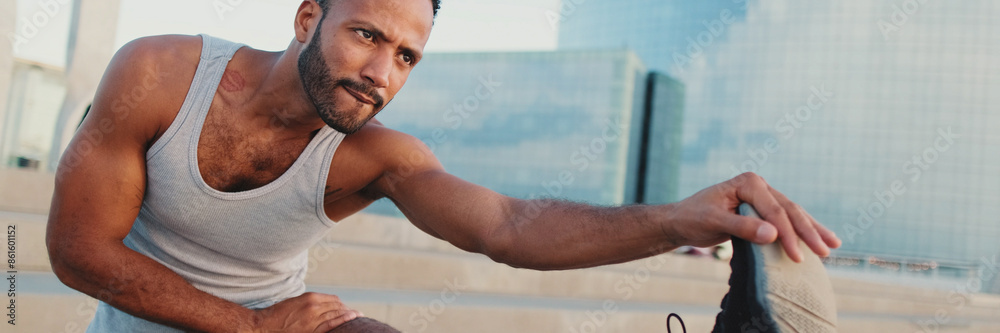 Close up, young bearded male athlete doing warm-up, stretching legs before training while standing on the embankment Close up, young bearded male athlete doing warm-up, stretching legs before training while standing on the embankment