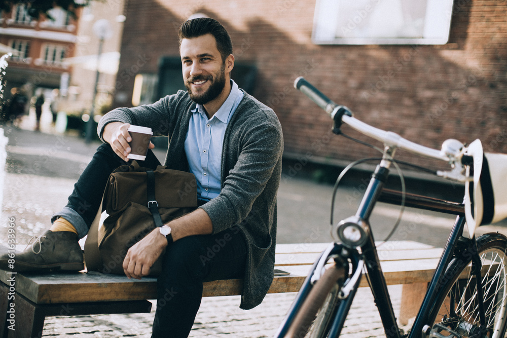 Relaxed stylish man sitting on bench with coffee next to bicycle in urban setting Relaxed stylish man sitting on bench with coffee next to bicycle in urban setting