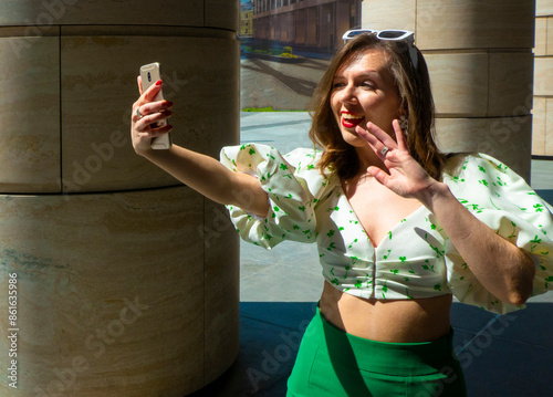 Obraz na płótnie Joyful young caucasian woman winks, bites her tongue, takes selfie on phone. Blonde model wears hat in sunny weather. Positive emotions concept. High quality photo w salonie