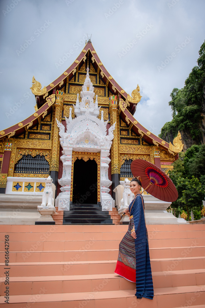Naklejka premium Woman wearing Thai dress visits beautiful temple in Thailand.