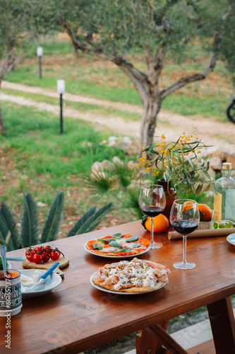 Outdoor Dining table of Homemade Pizza and Fresh Ingredients with wine and cutlery. Italian dream countryside olive garden romantic dinner 