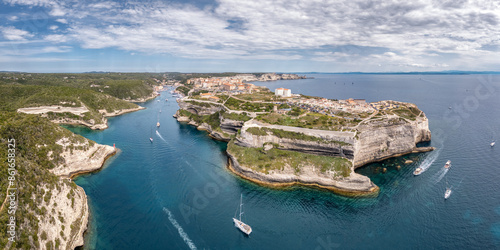 Panoramic aerial view of the limestone cliffs, harbour entrance and citadel of Bonifacio in Corsica with the coast of Sardinia in the distance