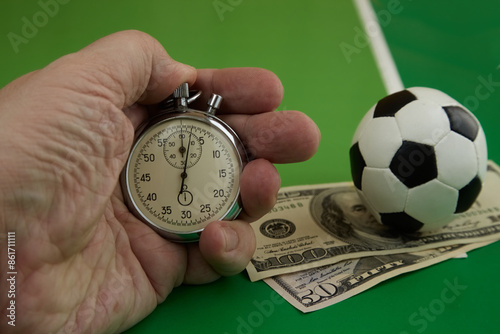 Photos stopwatch in hand and dollars with soccer ball on green background, bookmaker od