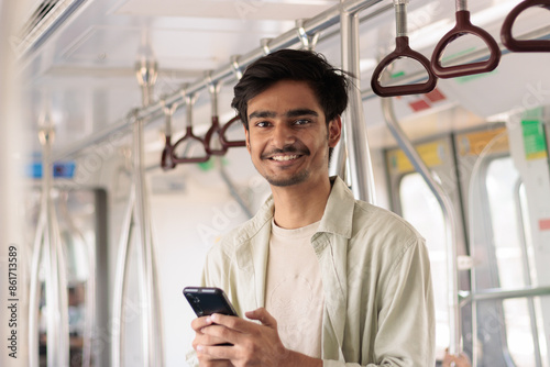 Portrait of young Indian man passenger traveling and using his smartphone in the metro or subway train. Metro and Public transportation concept.