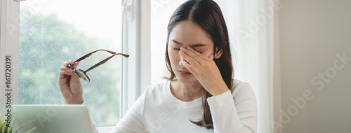 Eye problem concept, fatigue asian young woman tired eyes, irritated rubbing eye dry relief vision pain after work on laptop computer, eye strain, hand holding glasses, suffer migraine, bad blurry