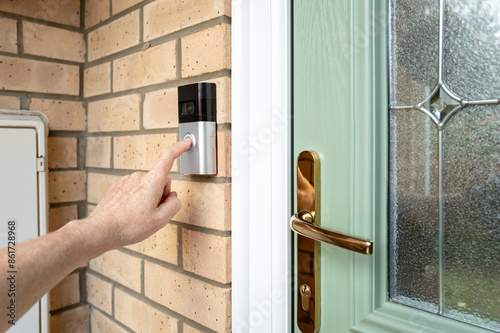 Visitor seen pressing the door bell button of a wireless smart home door bell which has an integrated camera and two-way audio. The door is a new, high security uPVC door.