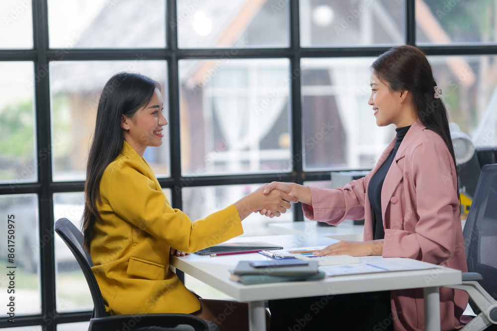 Obraz premium Two smiling businesswomen shaking hands after successful meeting in modern office