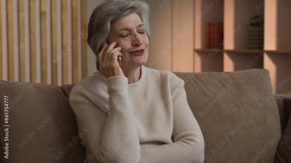 An elderly woman is sitting on the couch in her living room and talking ...