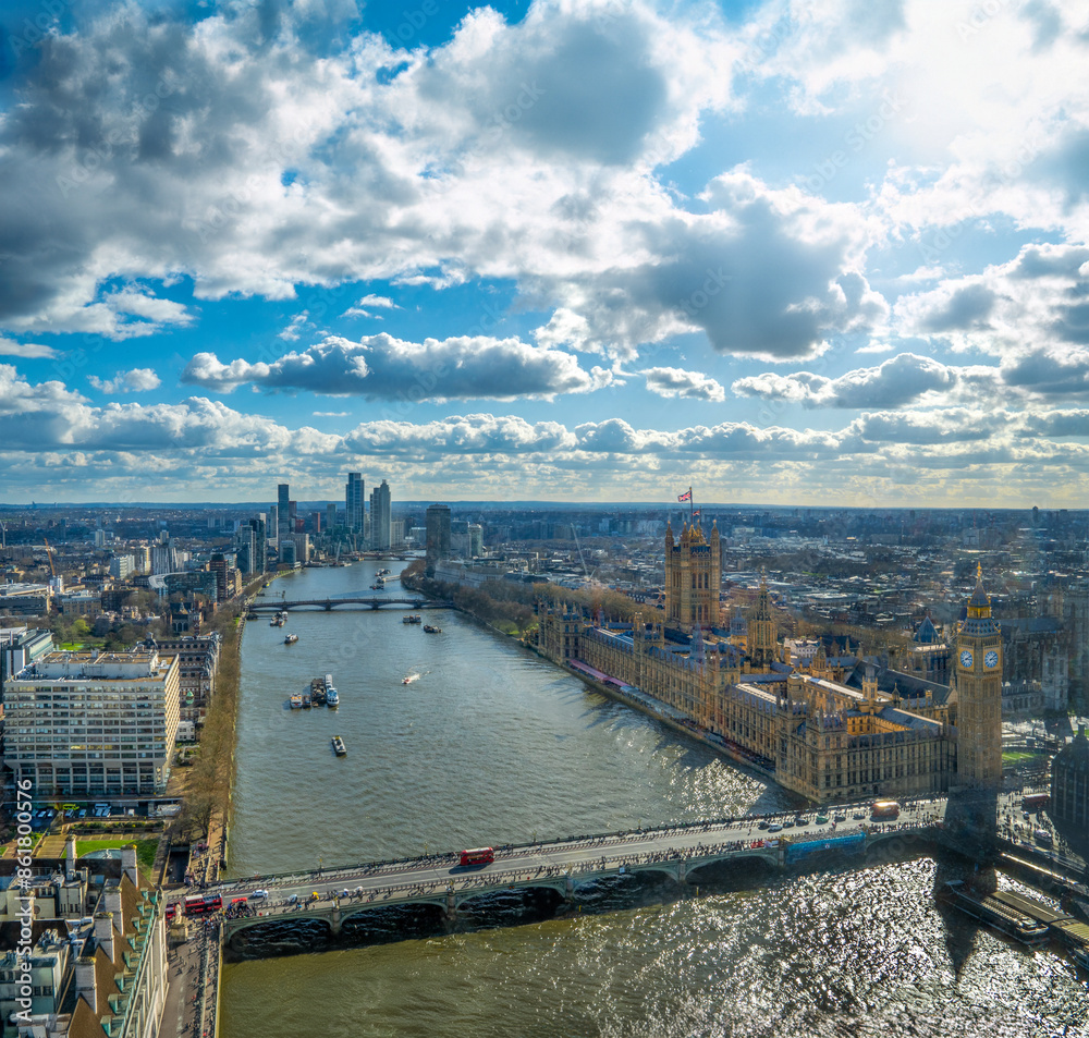 Obraz premium Panoramic aerial drone view of Westminster Abbey, Big Ben, House of Parliament and the River Thames at dusk with the city of London to the horizon under a sunny sky with backlit white clouds.
