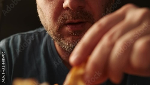 Close-up shot of a mans mouth as he reaches for a crispy, golden french fry photo