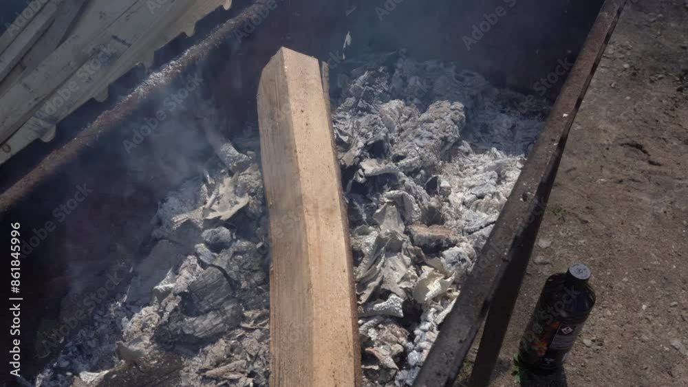 Valmiera, Latvia - June 23, 2024 - A close-up of a fire pit with smoldering ashes and a piece of wood, capturing the remnants of a fire in an outdoor setting. Copy space. Valmiera, Latvia - June 23, 2024 - A close-up of a fire pit with smoldering ashes and a piece of wood, capturing the remnants of a fire in an outdoor setting. Copy space.