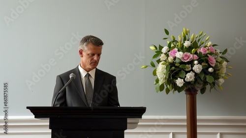 A man in a suit stands behind a podium giving a eulogy at a funeral photo