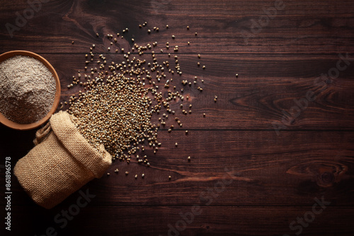 Bilde på lerret Organic whole Pearl Millet (Pennisetum glaucum) or Bajra seeds spilled out from a laying jute bag with Bajra Flour, isolated on a dark wooden background