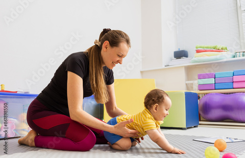 Physical therapist assisting young child with damage to nervous system at rehabilitation center during daytime. Specialist aids little boy in body motor skill development photo