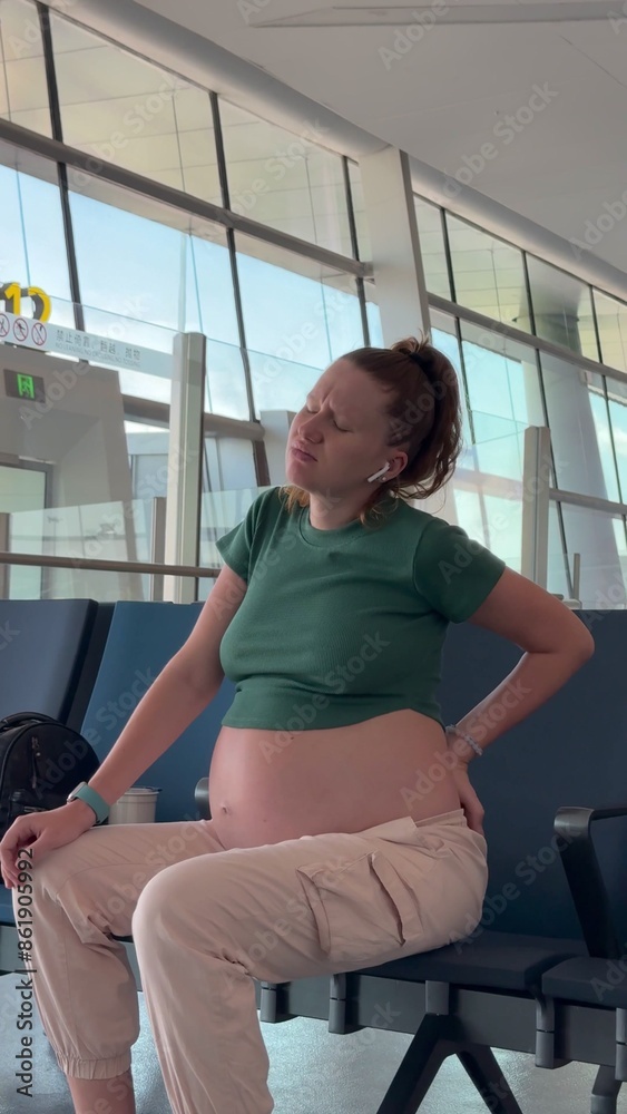 pregnant woman sitting on a chair, suffering from lower back pain, back problems, public place, airport, health pregnant woman sitting on a chair, suffering from lower back pain, back problems, public place, airport, health