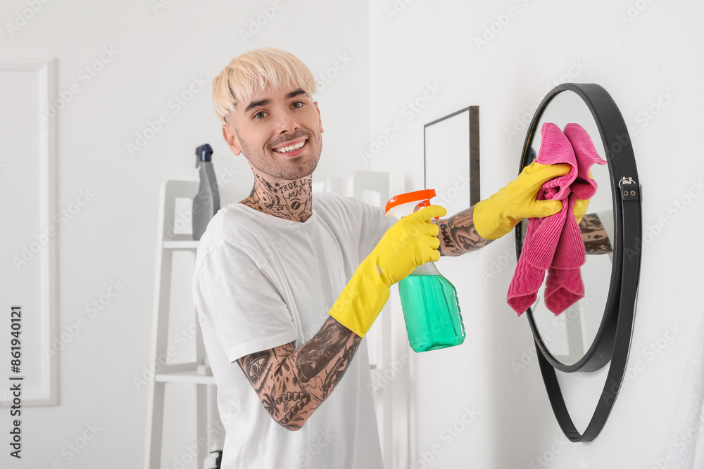Young tattooed man cleaning mirror in bathroom Young tattooed man cleaning mirror in bathroom