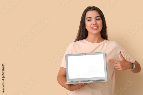 Happy young female programmer pointing at laptop on beige background