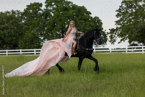 Horse Girl princess with black friesian  horse and pink romantic dress in a green field