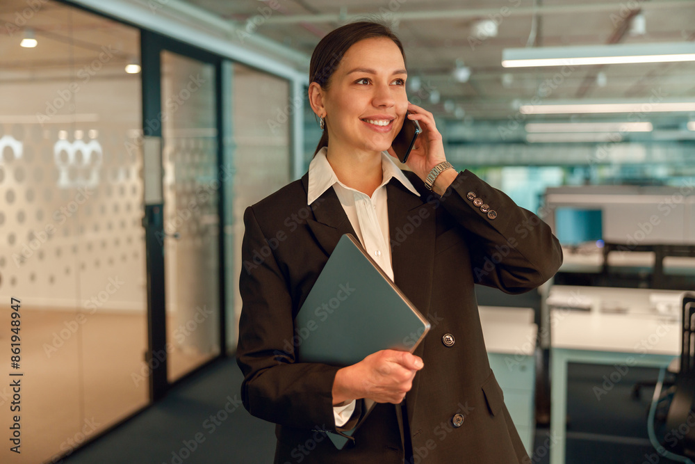 A professional businesswoman in a modern office, on a call and holding important documents A professional businesswoman in a modern office, on a call and holding important documents