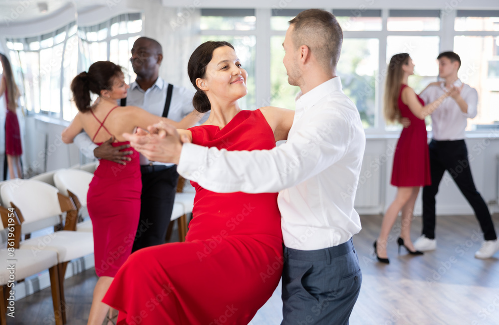 Obraz premium Smiling young woman in red dress and her partner successfully perform mesmerizing movements of paso doble dance during dance party