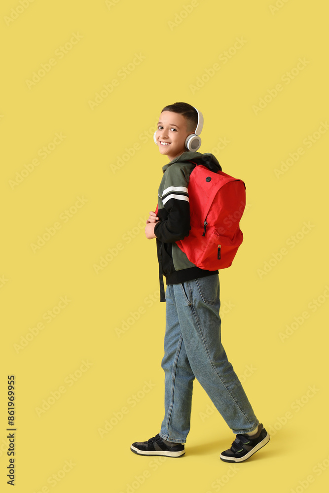 Fototapeta premium Cute schoolboy with headphones and backpack on yellow background