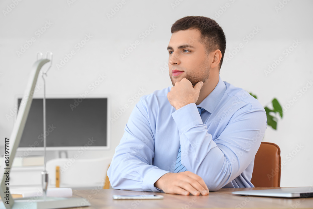 Naklejka premium Thoughtful young businessman pondering business strategy and future decisions in a modern office environment, he is focused on his thoughts, with his hand resting on his chin