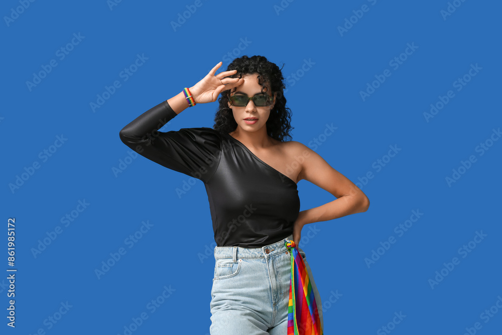 Young African-American woman with rainbow flag and stylish sunglasses on blue background. LGBT concept Young African-American woman with rainbow flag and stylish sunglasses on blue background. LGBT concept