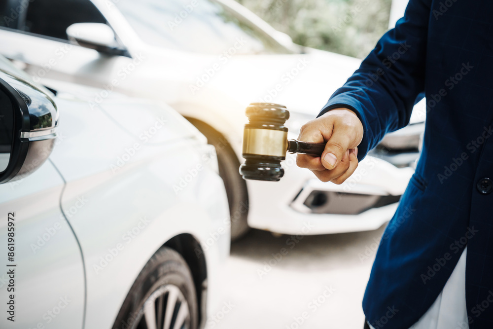 Fototapeta premium businessman in a suit and a lawyer, holding a wooden gavel, stand in front of a car, discussing legal aspects like citations, liability, and negligence related to a traffic violation...