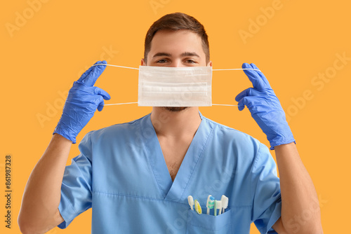 Male dentist with medical mask on yellow background