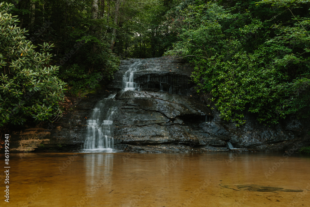 Beautiful large waterfall between green trees in the mountains. Mountain landscape with a waterfall on a summer day. Wildcat Waterfall, Great Smokey Mountains, South Carolina, USA. Beautiful large waterfall between green trees in the mountains. Mountain landscape with a waterfall on a summer day. Wildcat Waterfall, Great Smokey Mountains, South Carolina, USA.