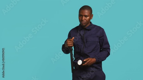Portrait of security guard overseeing premises, turning on flashlight and preparing baton to detain suspects. Private law enforcement worker using lantern and truncheon gear, studio backdrop, camera B photo