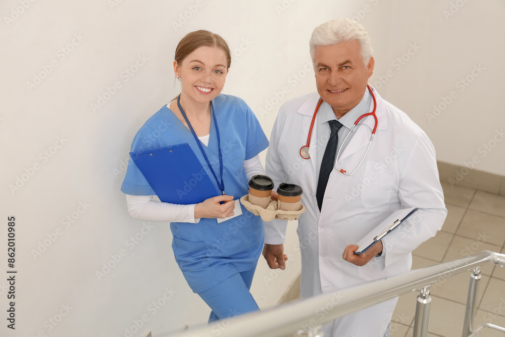 Mature doctor and nurse with coffee on stairs in clinic Mature doctor and nurse with coffee on stairs in clinic