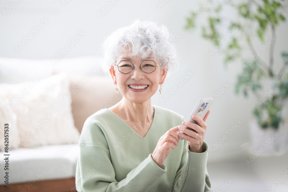 スマートフォン(スマホ)を持つタップする笑顔のシニア(高齢者)女性のカメラ目線 タップや操作する スマートフォン(スマホ)を持つタップする笑顔のシニア(高齢者)女性のカメラ目線 タップや操作する