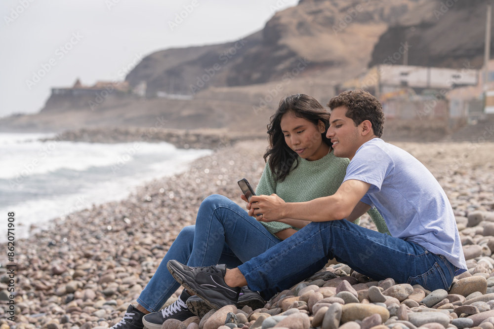 Couple sitting on the beach using phone Couple sitting on the beach using phone