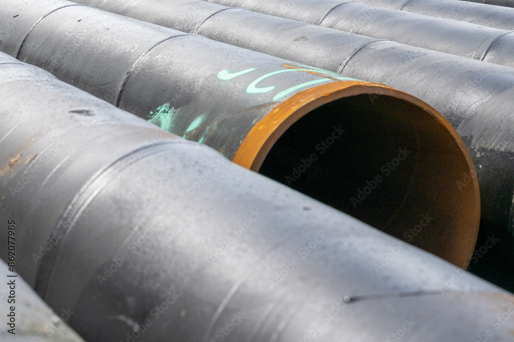 Rows of large black hollow drilling pipes. The ends are rusty on the thin-walled steel piping. The heavy industrial pipe is used for drilling in mining, pipe lines, oil rigs, and wharves and piers. Rows of large black hollow drilling pipes. The ends are rusty on the thin-walled steel piping. The heavy industrial pipe is used for drilling in mining, pipe lines, oil rigs, and wharves and piers.
