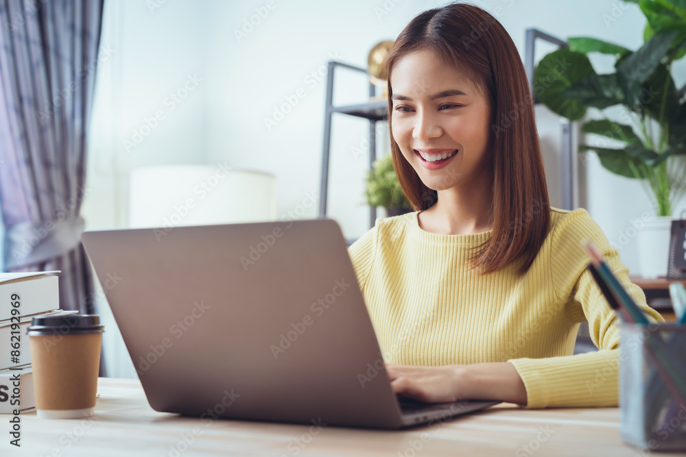 Cheerful beautiful Asian woman sitting at the desk and using laptop computer. Cheerful beautiful Asian woman sitting at the desk and using laptop computer.